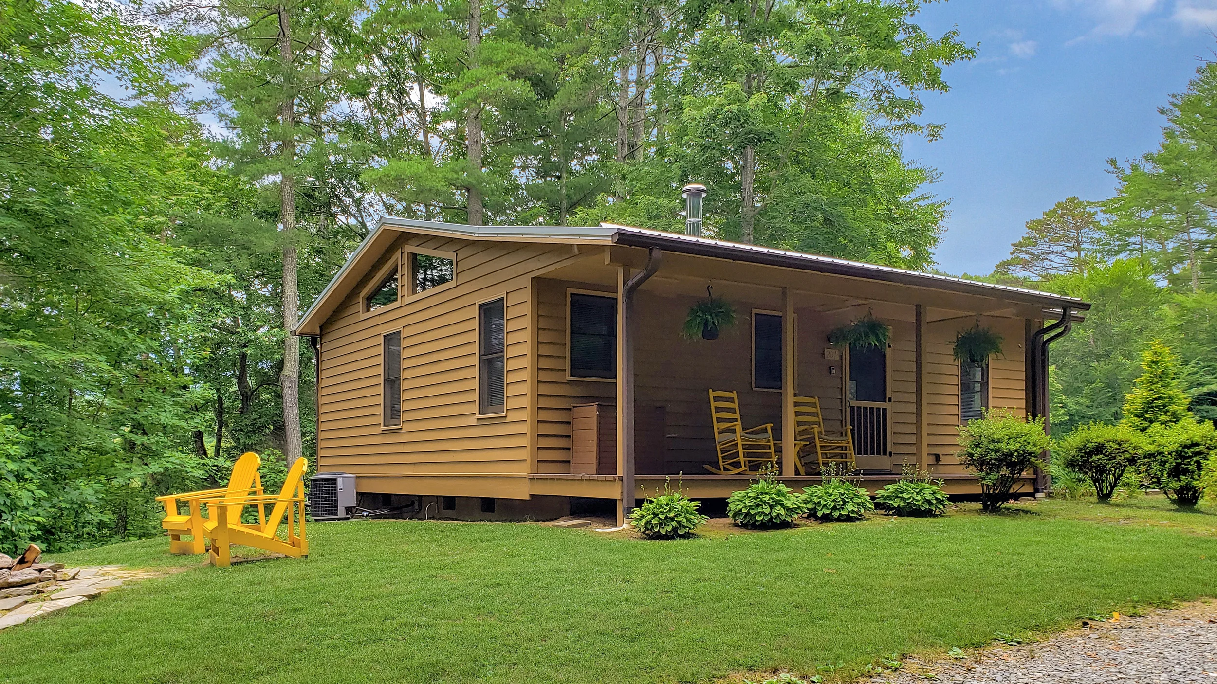 A cabin in the woods with yellow rocking chairs on the covered porch